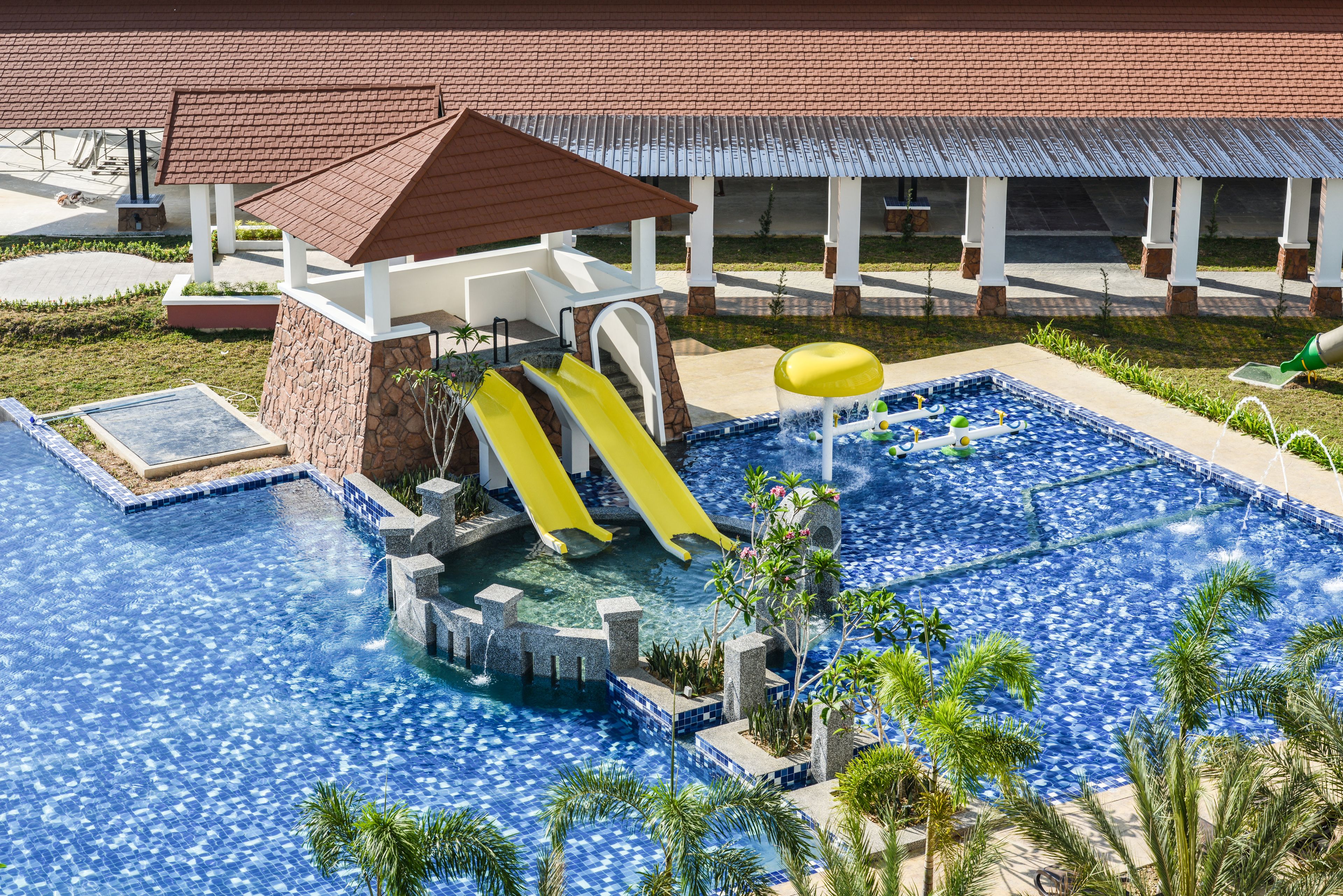 A swimming pool with a slide, a water fountain, and a covered area with a roof.