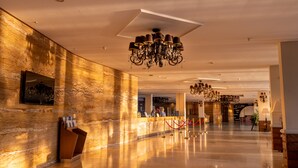 Un hall d’entrée spacieux aux murs de marbre, avec un comptoir de réception et des lustres.