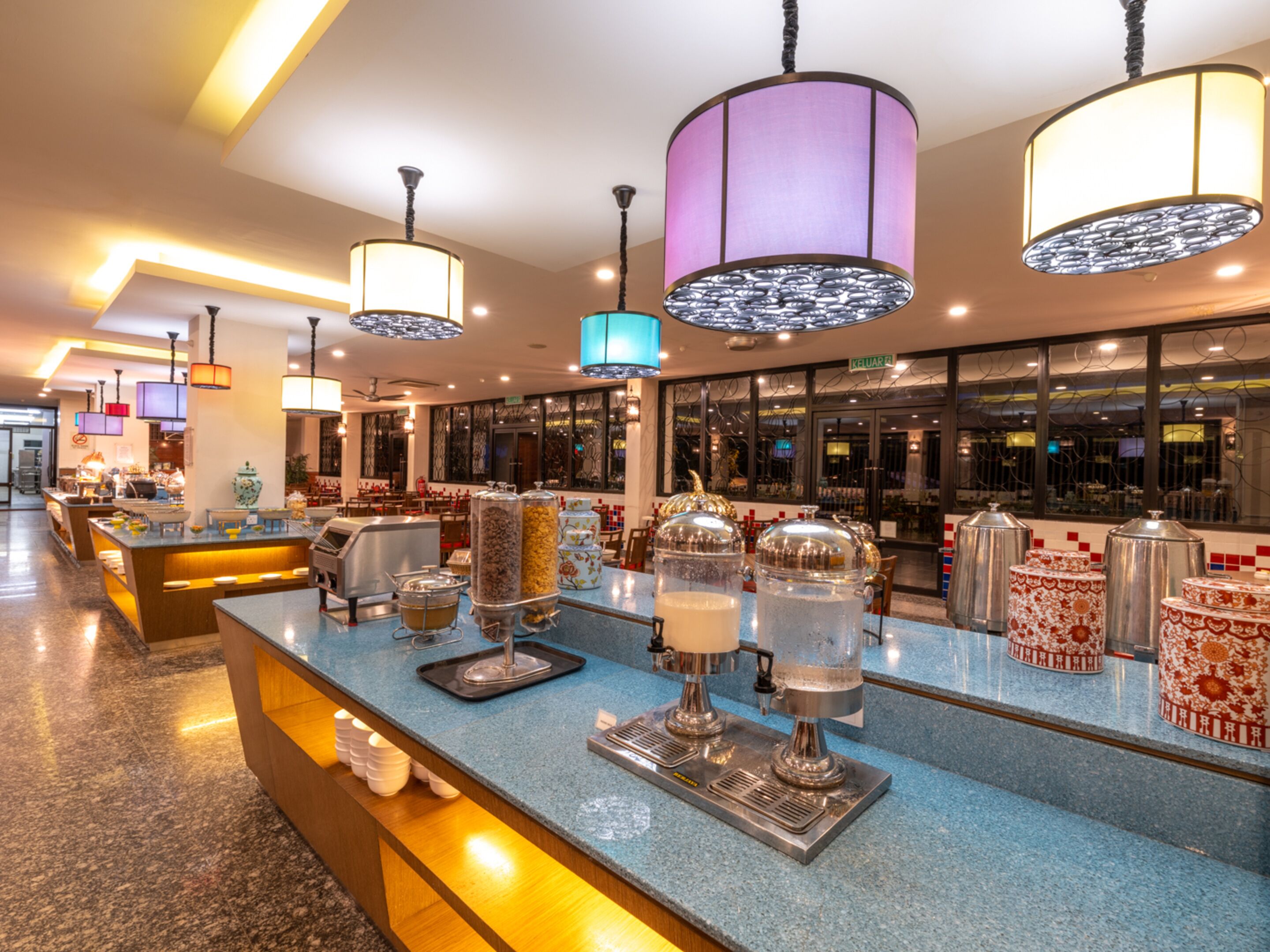 A modern hotel lobby with a self-service beverage station, a seating area, and a view of the street outside.