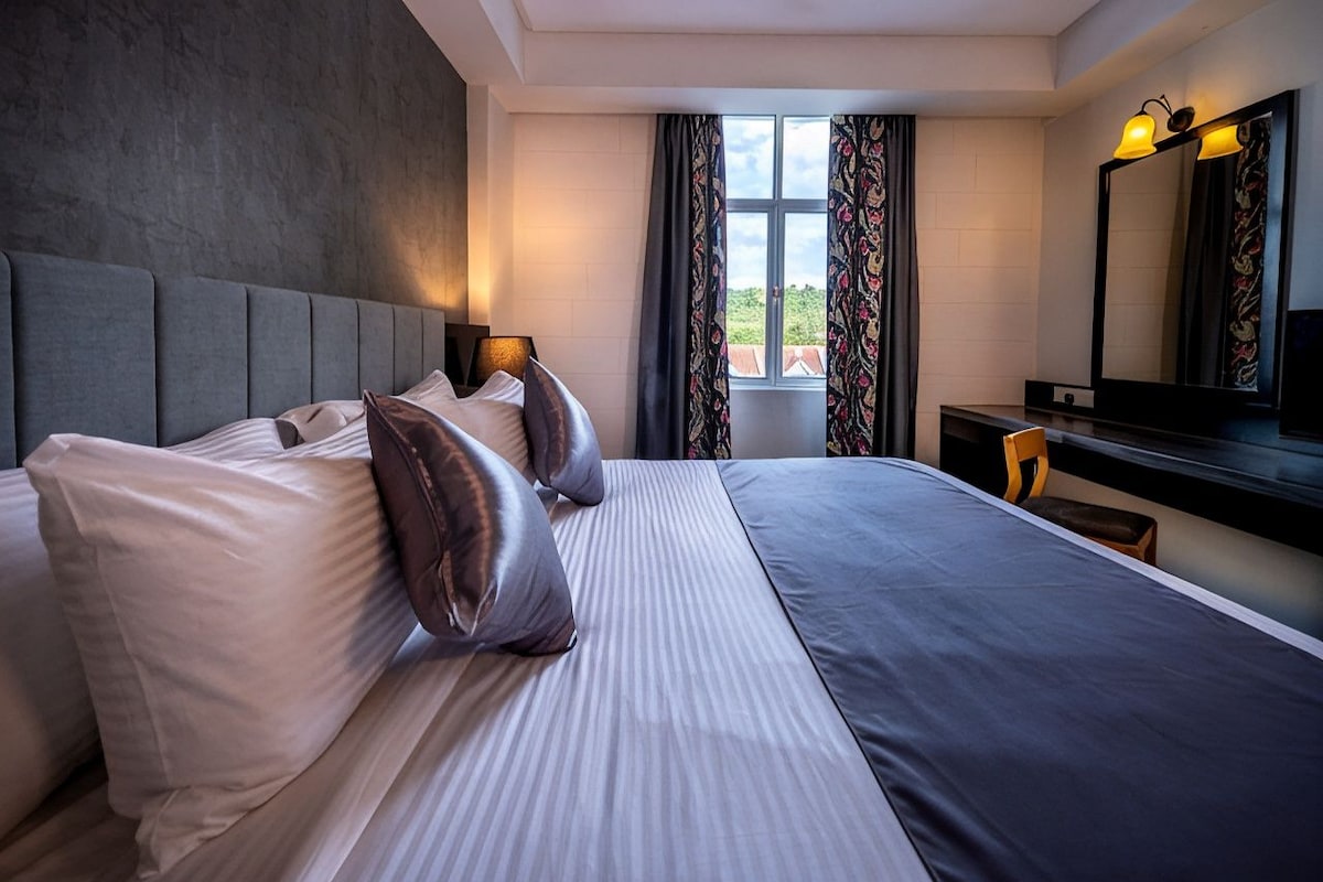 Ein Hotelzimmer mit einem großen Bett, einem Nachttisch, einem Spiegel und einem Fenster mit Vorhängen.