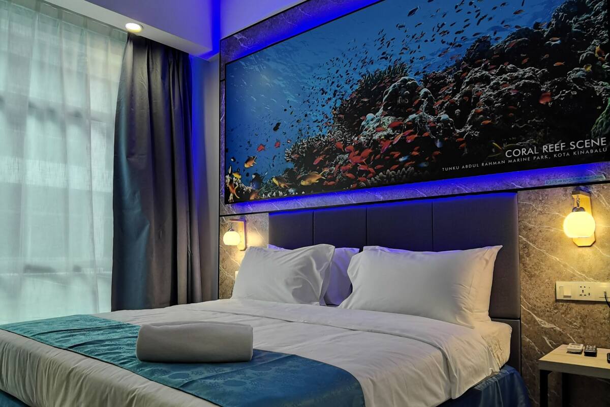 A modern hotel room with a large bed, a nightstand, and a wall-mounted TV displaying a coral reef scene.