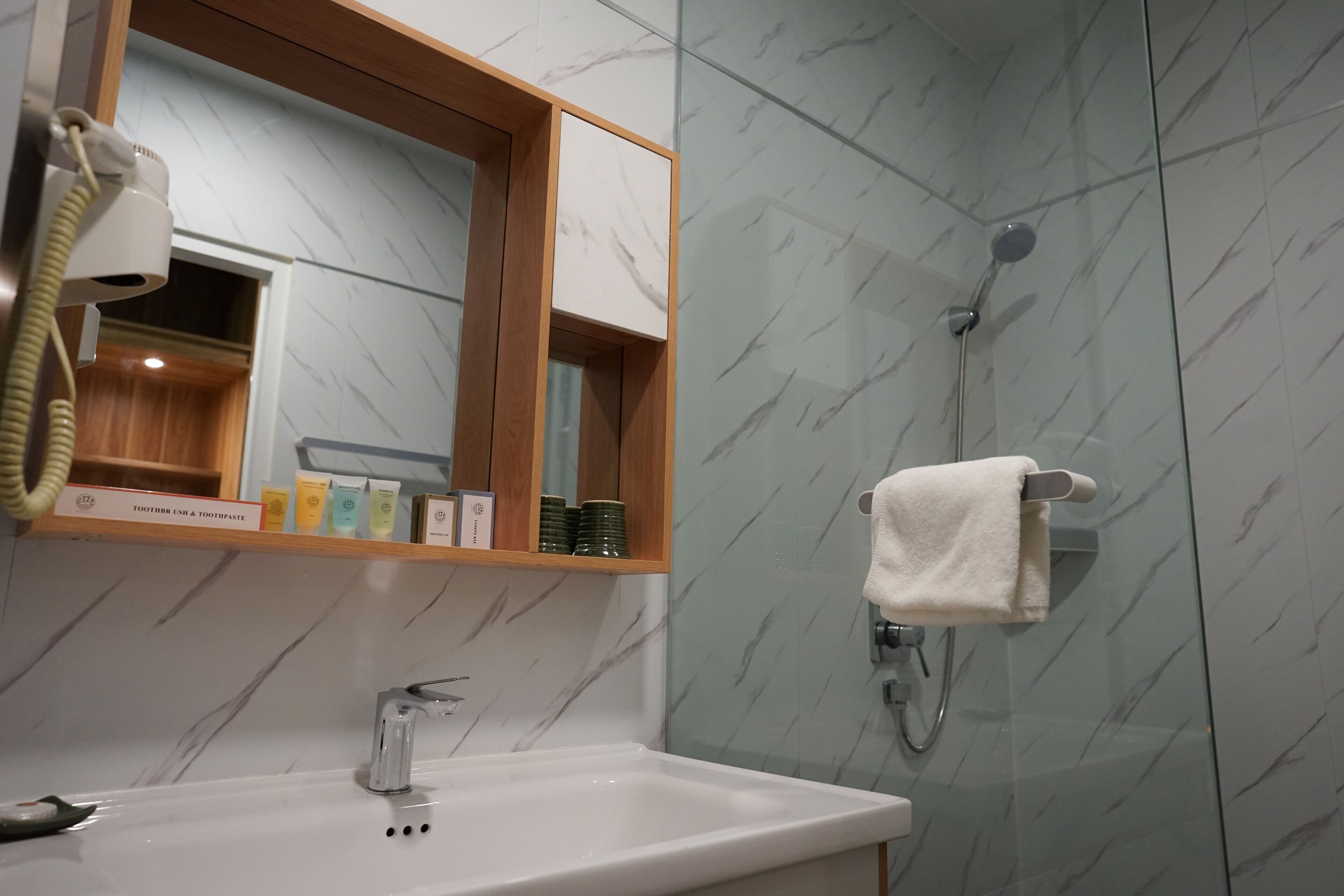 A bathroom with a marble-tiled shower, a white sink, and a mirror with a wooden frame.