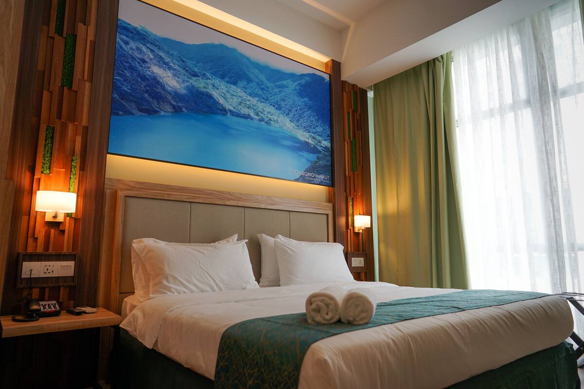 A hotel room with a large bed, a nightstand with a lamp, and a large painting above the bed.