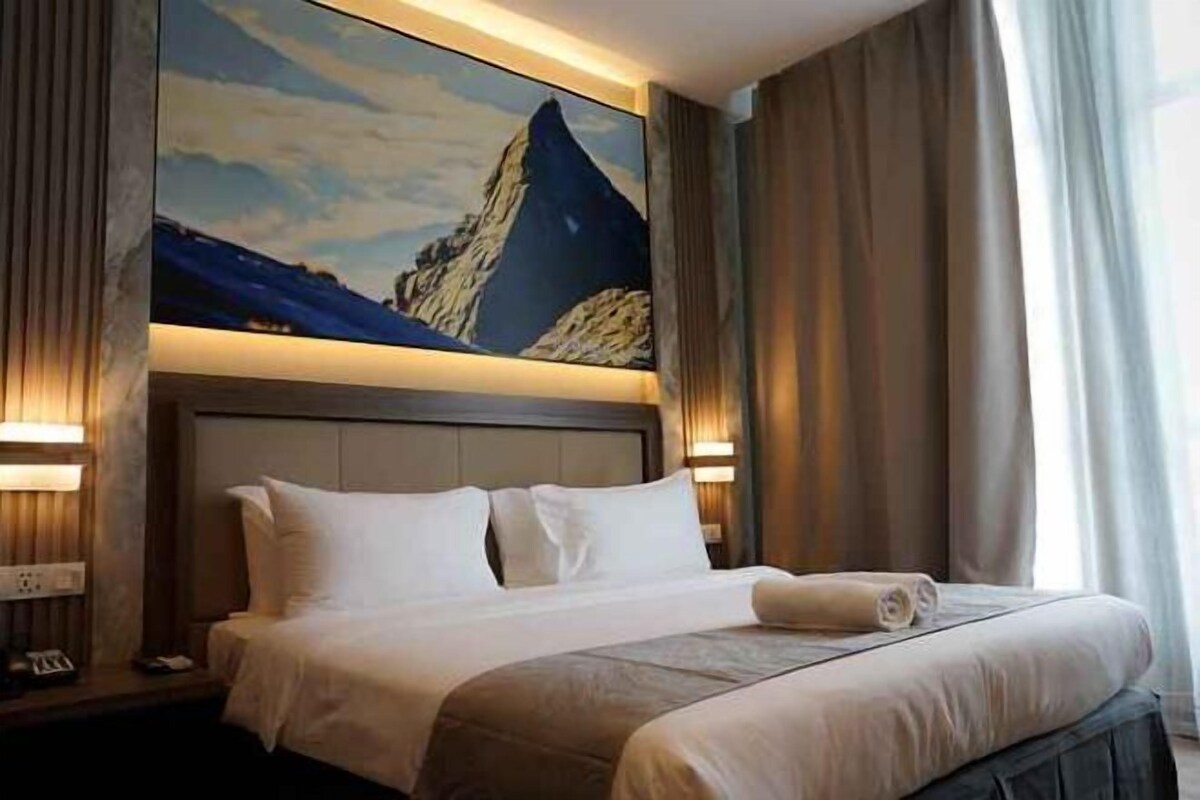 A hotel room with a large bed, a headboard with a painting, and a nightstand with a lamp.