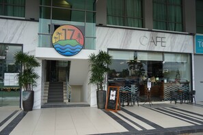 A cafe with a large sign, outdoor seating, and a staircase leading to the entrance.