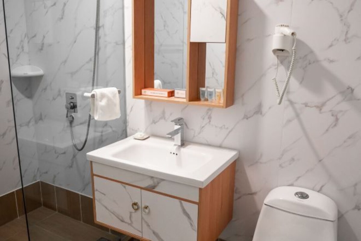 Ein Badezimmer mit Marmorwand, einem weißen Waschbecken, einem Holzkabinent und einer Toilette. Ein Spiegel mit einem darüberhängenden Handtuch.