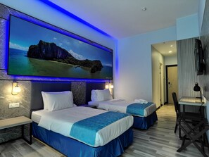 Ein Hotelzimmer mit zwei Betten, einem großen, an der Wand montierten Fernseher, der einen schönen Ausblick zeigt, einem Schreibtisch mit Stuhl und einer Tür zu einem anderen Raum.