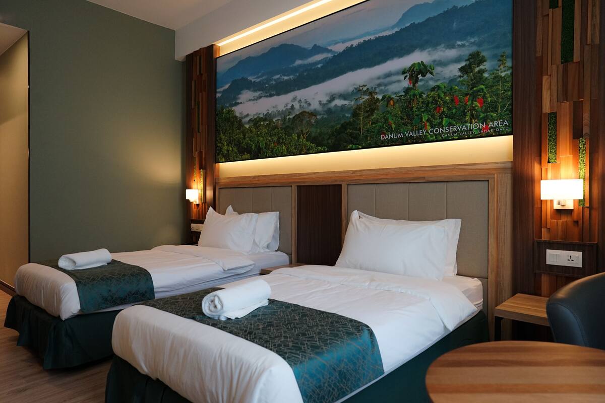 A hotel room with two beds, a large wall mural, and a wooden headboard.