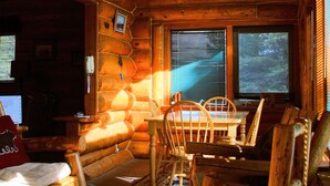 Interior de una cabaña de troncos con una mesa de comedor de madera, sillas y una chimenea.