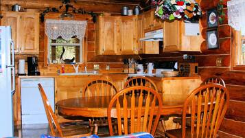 A wooden cabin interior with a dining table, chairs, a refrigerator, and a window with a view.