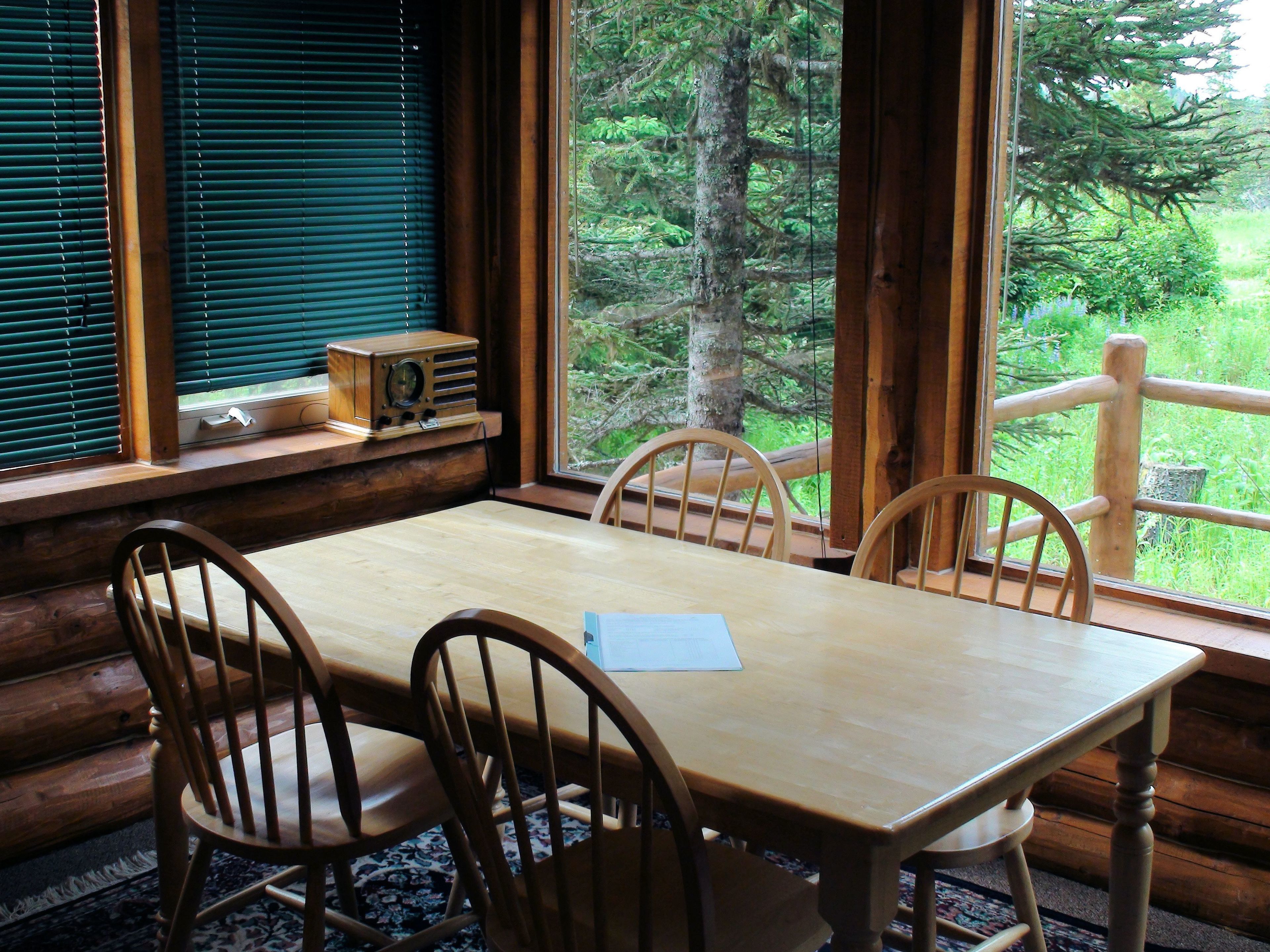 A wooden dining table with four chairs, a window with blinds, and a radio on the windowsill.
