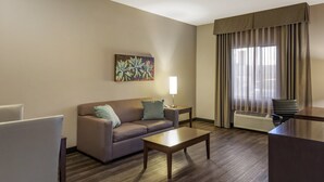 A hotel room with a sofa, a coffee table, a lamp, a chair, and a large window with curtains. - Holiday Inn Express & Suites Indio - Coachella Valley by IHG (Indio)