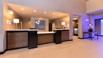 Ein Hotel-Empfangsbereich mit modernem Design, der einen Empfangstresen, eine digitale Anzeige und einen Kühlschrank umfasst.
