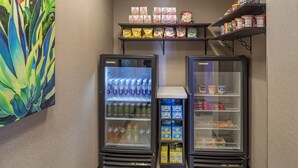 Two beverage dispensers, a snack shelf, and a refrigerated display with various food items. - Holiday Inn Express & Suites Indio - Coachella Valley by IHG (Indio)