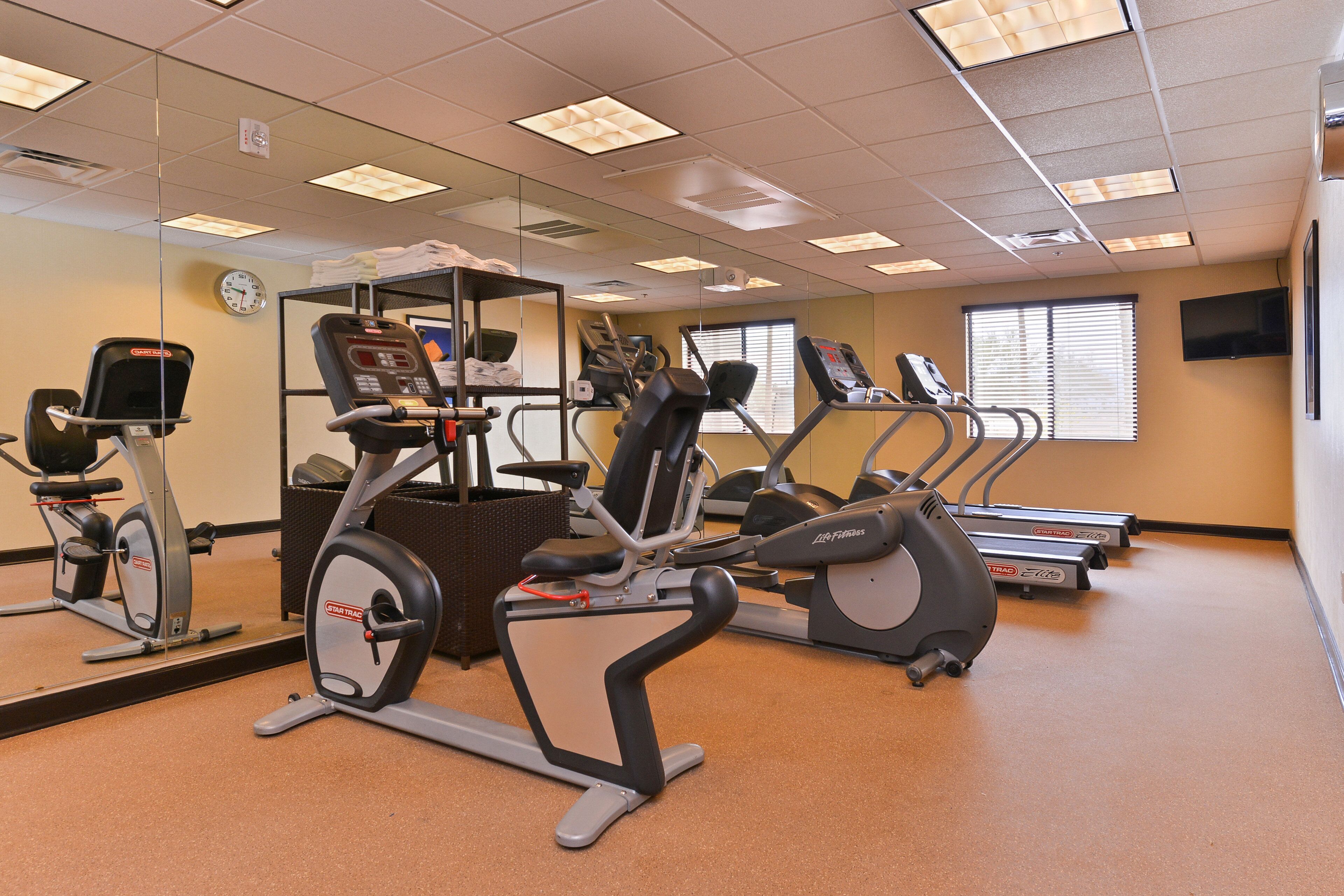 A fitness center with various exercise machines, a clock, and a television on the wall.