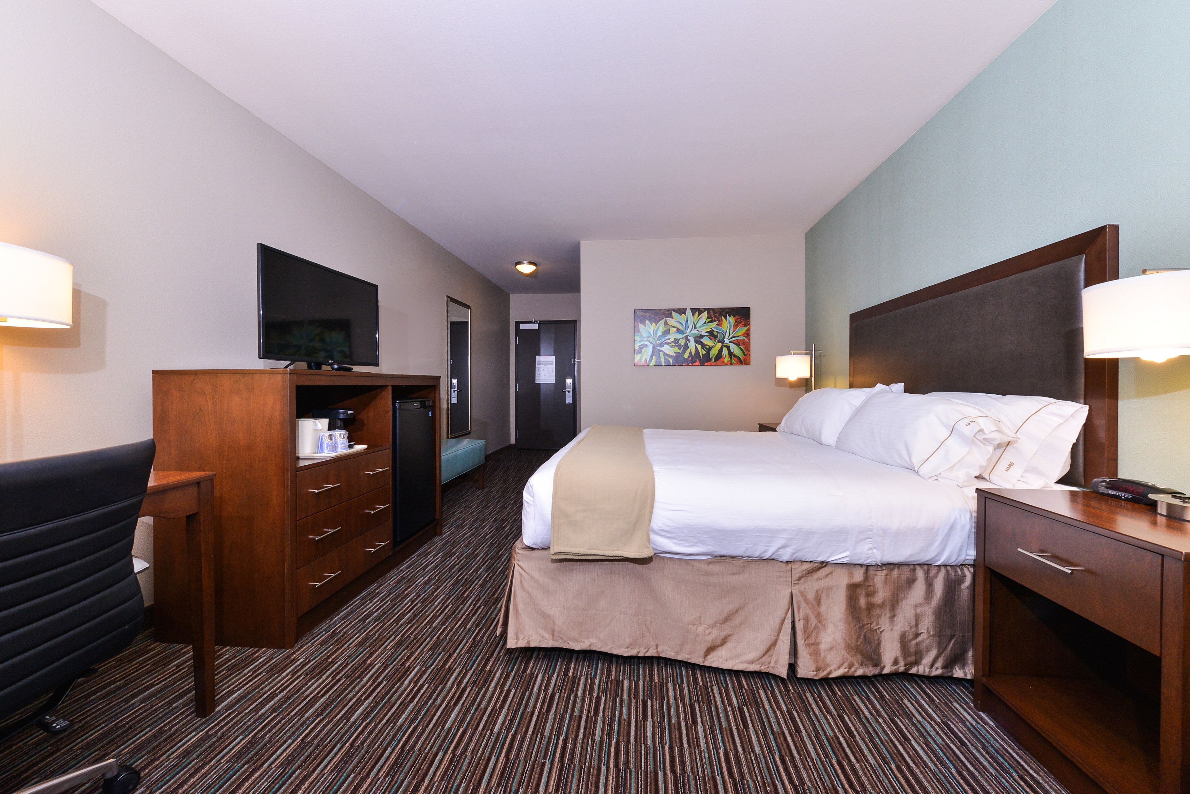 A hotel room with a bed, bedside table, desk, chair, television, and a painting on the wall.