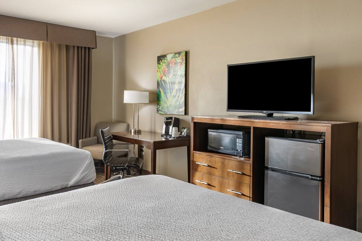 A hotel room with two beds, a desk with a computer, a television, a refrigerator, and a painting on the wall.