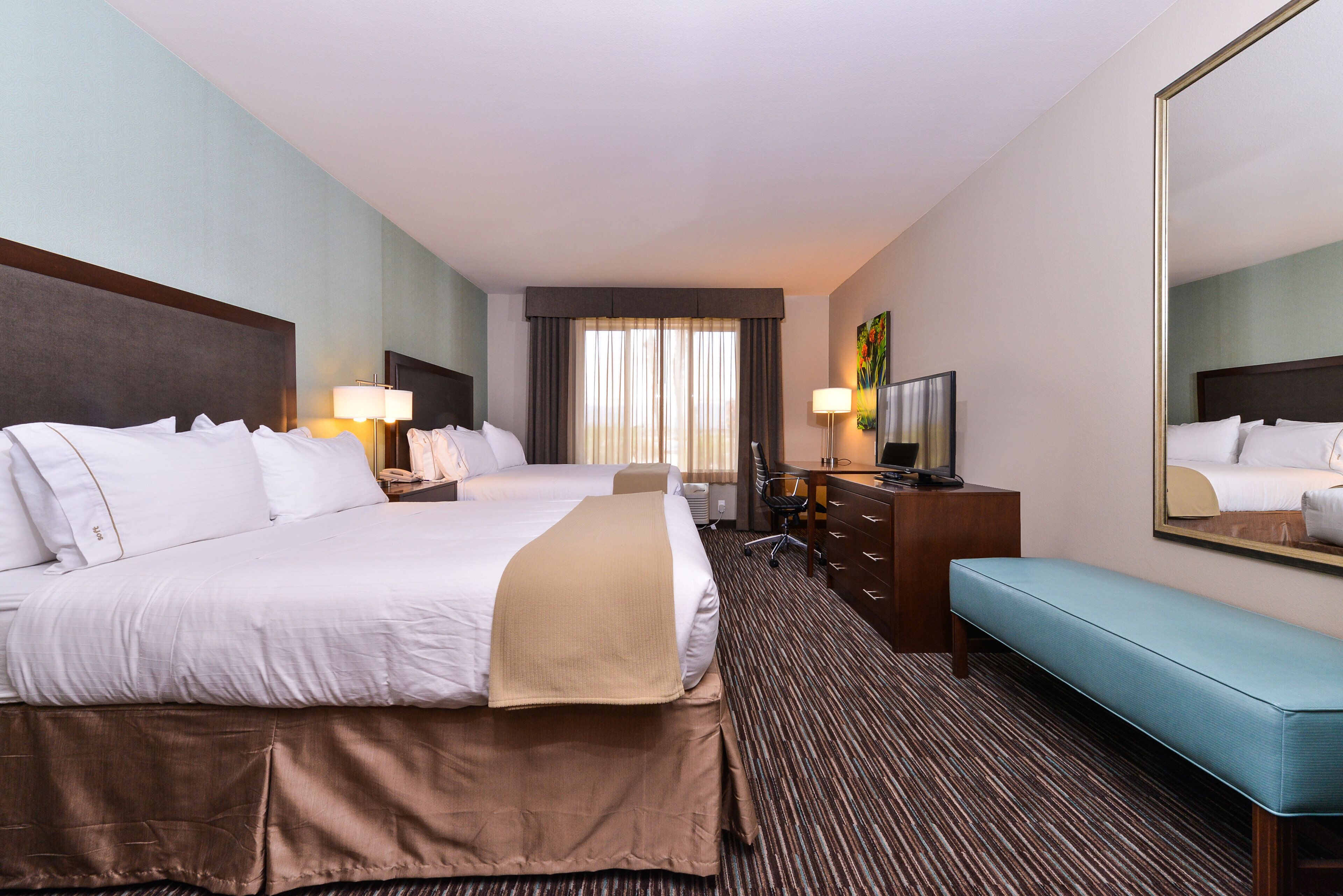 Une chambre d’hôtel avec deux lits, un bureau, une chaise, une télévision et un grand miroir.