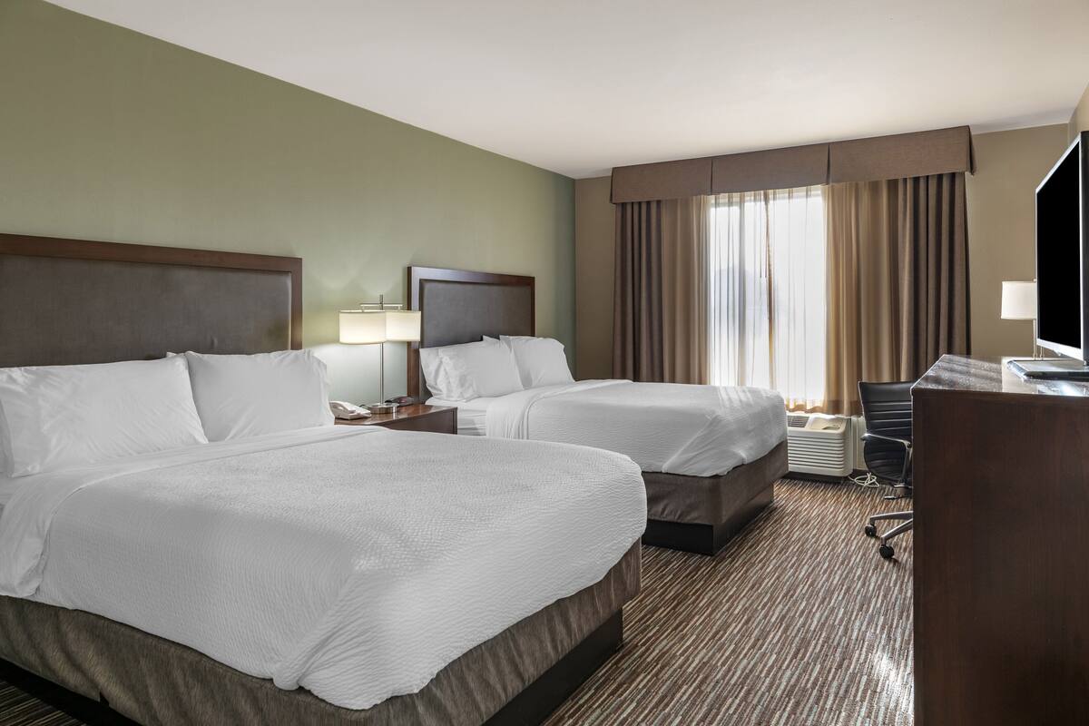 A hotel room with two beds, a desk, a chair, and a television.