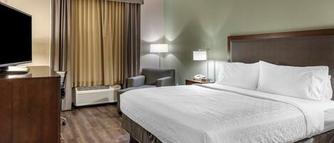 A hotel room with a large bed, a desk with a flat-screen TV, a chair, a lamp, and a telephone.