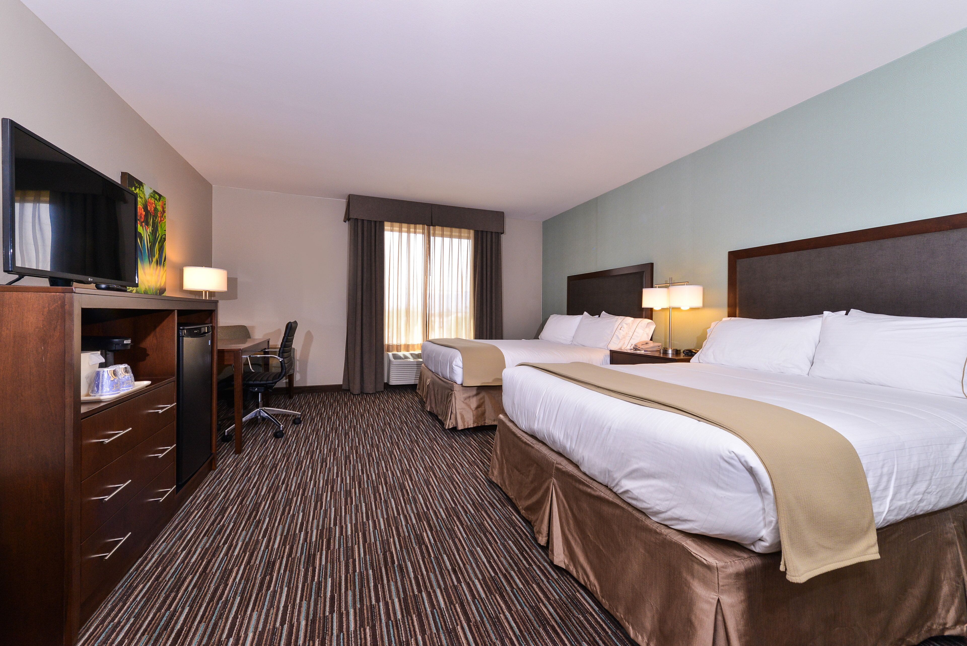 A hotel room with two beds, a desk, a television, and a window with curtains.