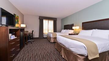 A hotel room with two beds, a desk, a television, and a window with curtains.