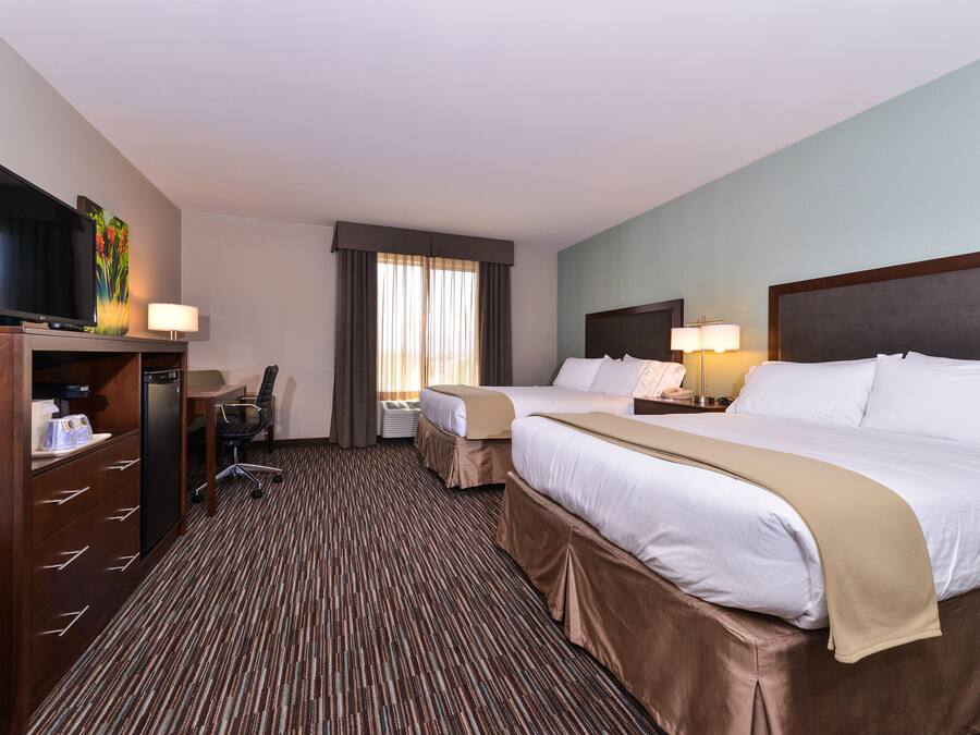 A hotel room with two beds, a desk, a television, and a window with curtains.