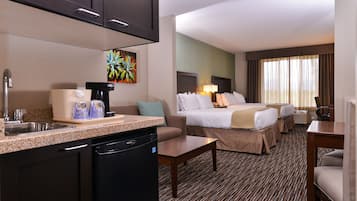 Habitación de hotel con kitchenette, una cama con dos almohadas, una mesita de noche y una ventana con cortinas.