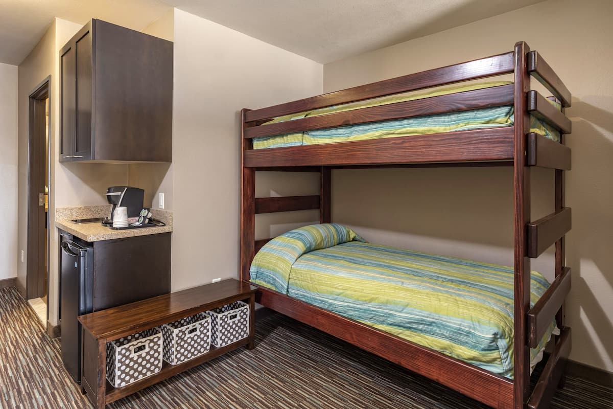 A bunk bed with a wooden frame, a small desk with a coffee maker, and a patterned rug.
