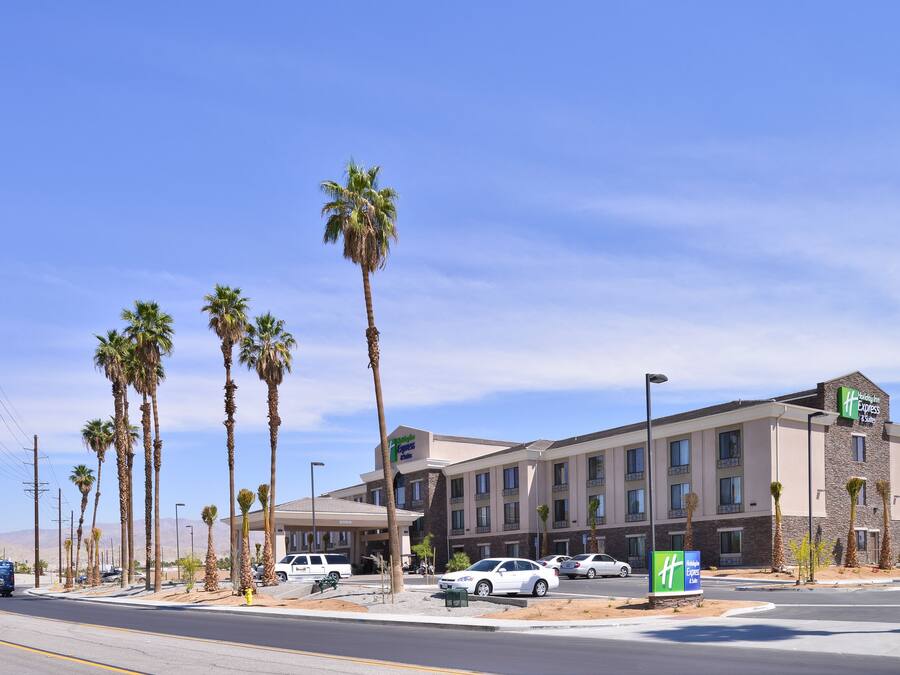 A Holiday Inn Express hotel with a parking lot, palm trees, and a clear blue sky.