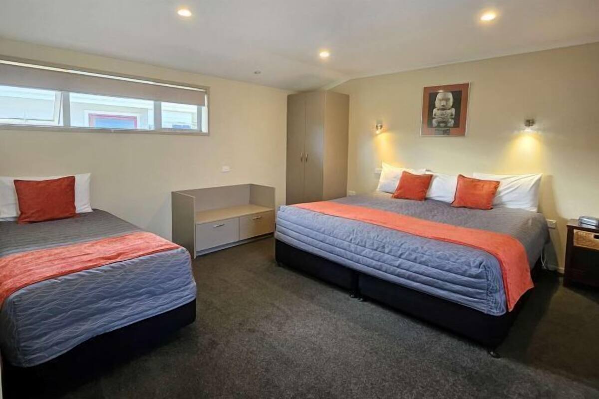 Quarto de hotel com duas camas, um guarda-roupa, um espaço de estar pequeno e uma estátua na parede.