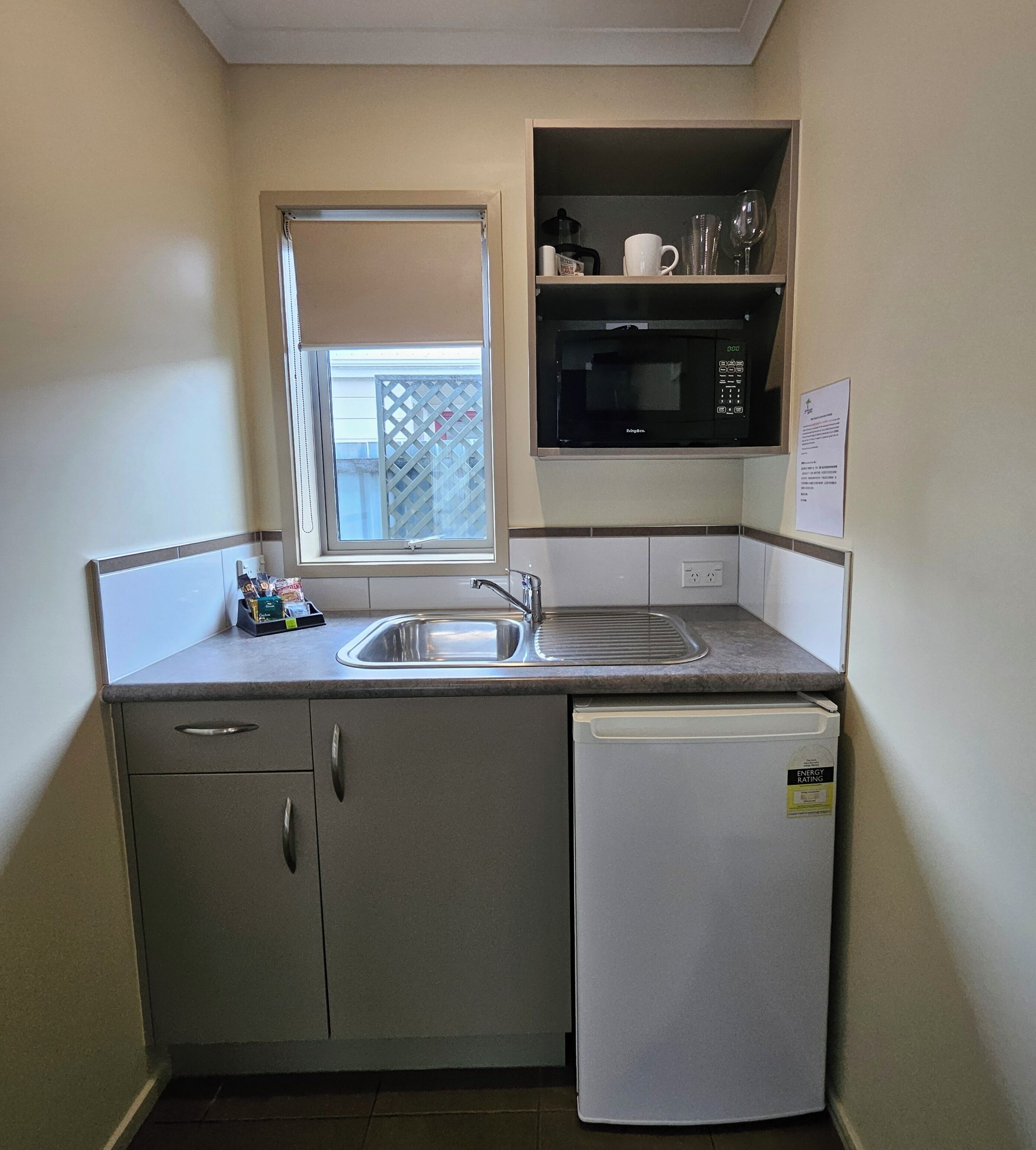 A compact kitchen with a sink, a microwave, a refrigerator, and a window with a view of a fence.