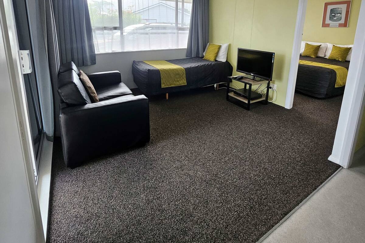 Quarto de hotel com sofá, cama, televisão e janela com cortinas.