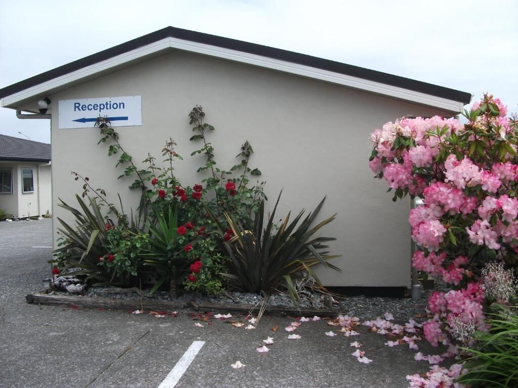 A building with a reception sign, surrounded by flowering plants and a paved area.