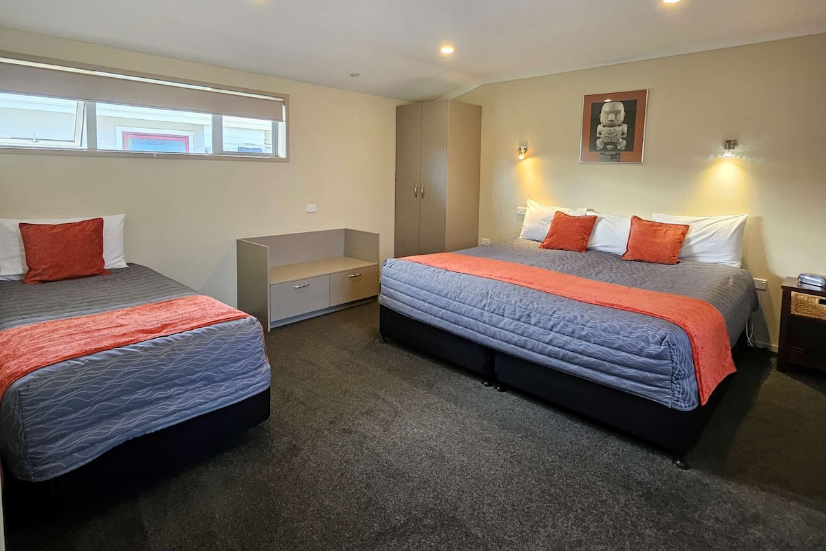 Quarto com duas camas, um banco, um guarda-roupa e um quadro na parede.