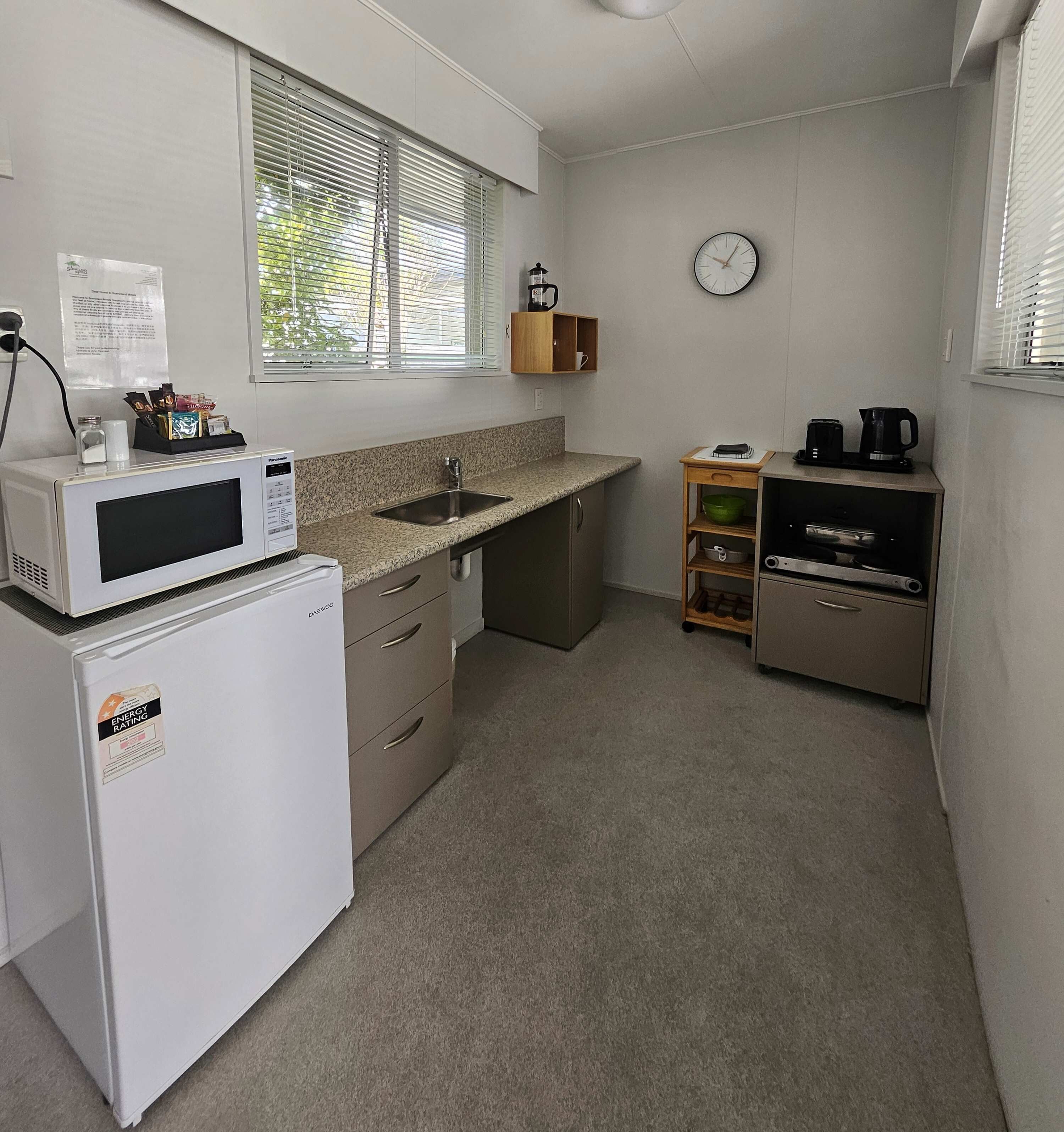 Cocina compacta con microondas, refrigerador, pileta y una pequeña cafetera.