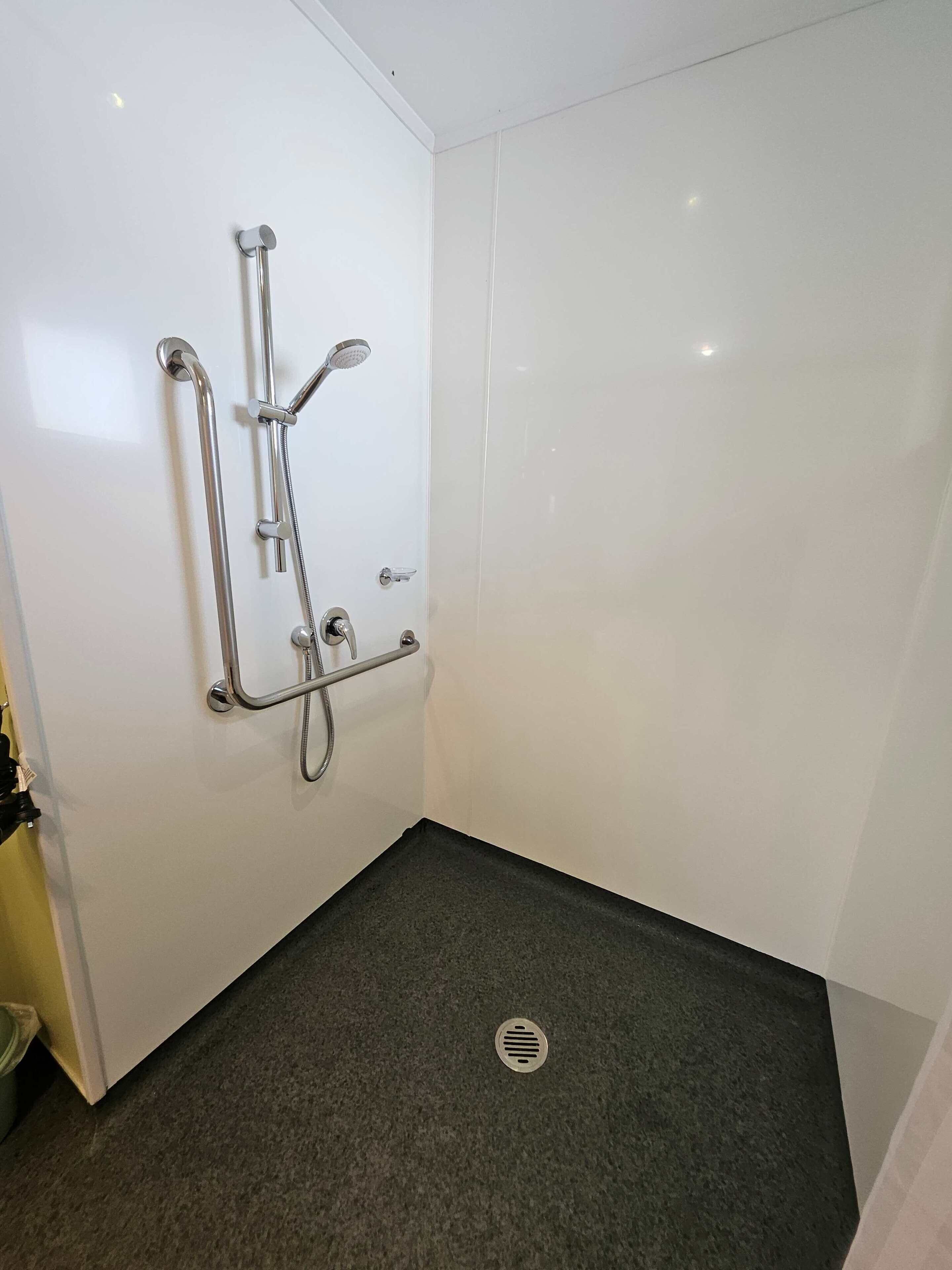 A small, white-walled bathroom with a shower, grab bar, and a floor drain.