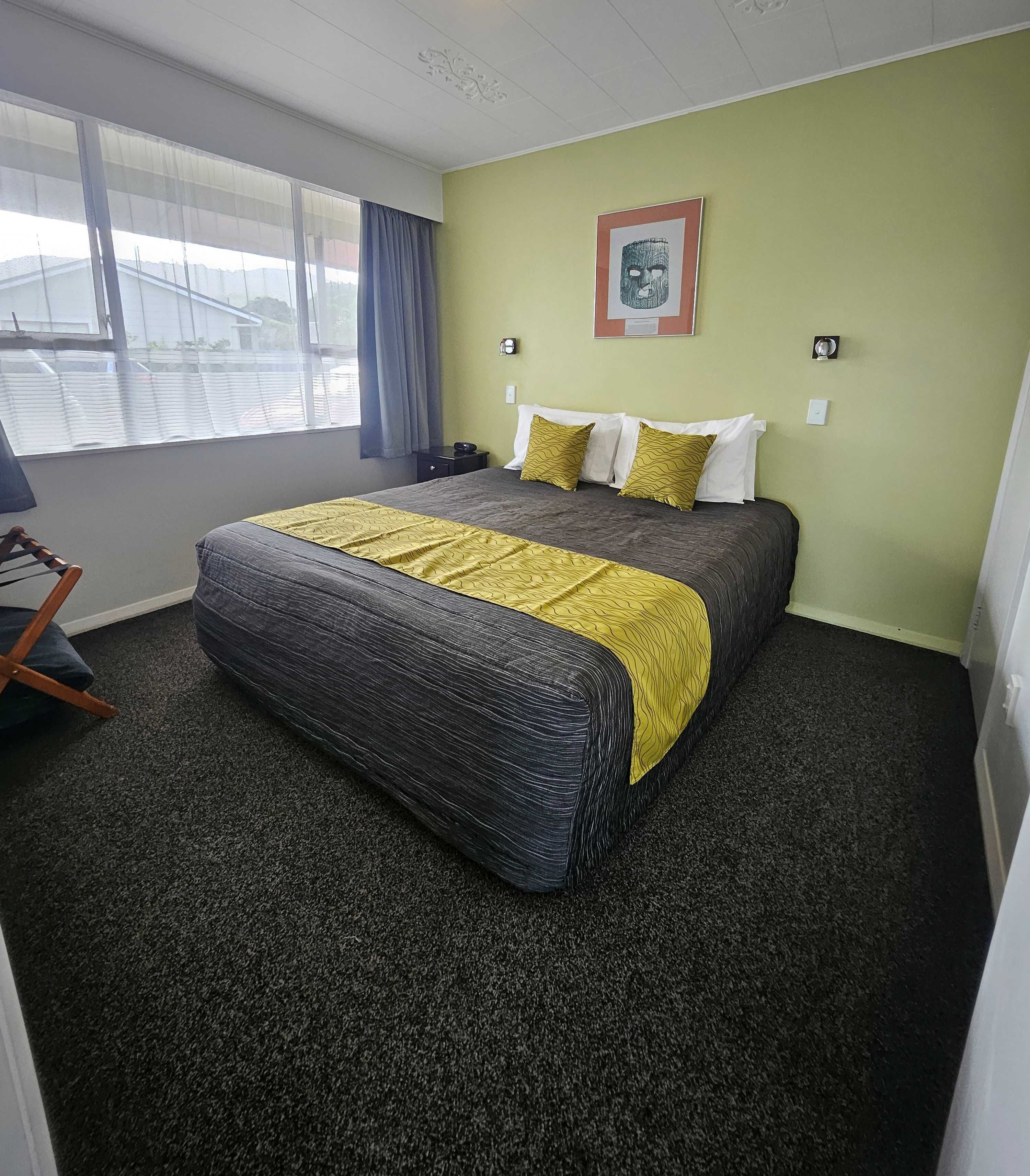 Quarto de hotel com cama, uma cadeira, janela com cortinas e um quadro na parede.