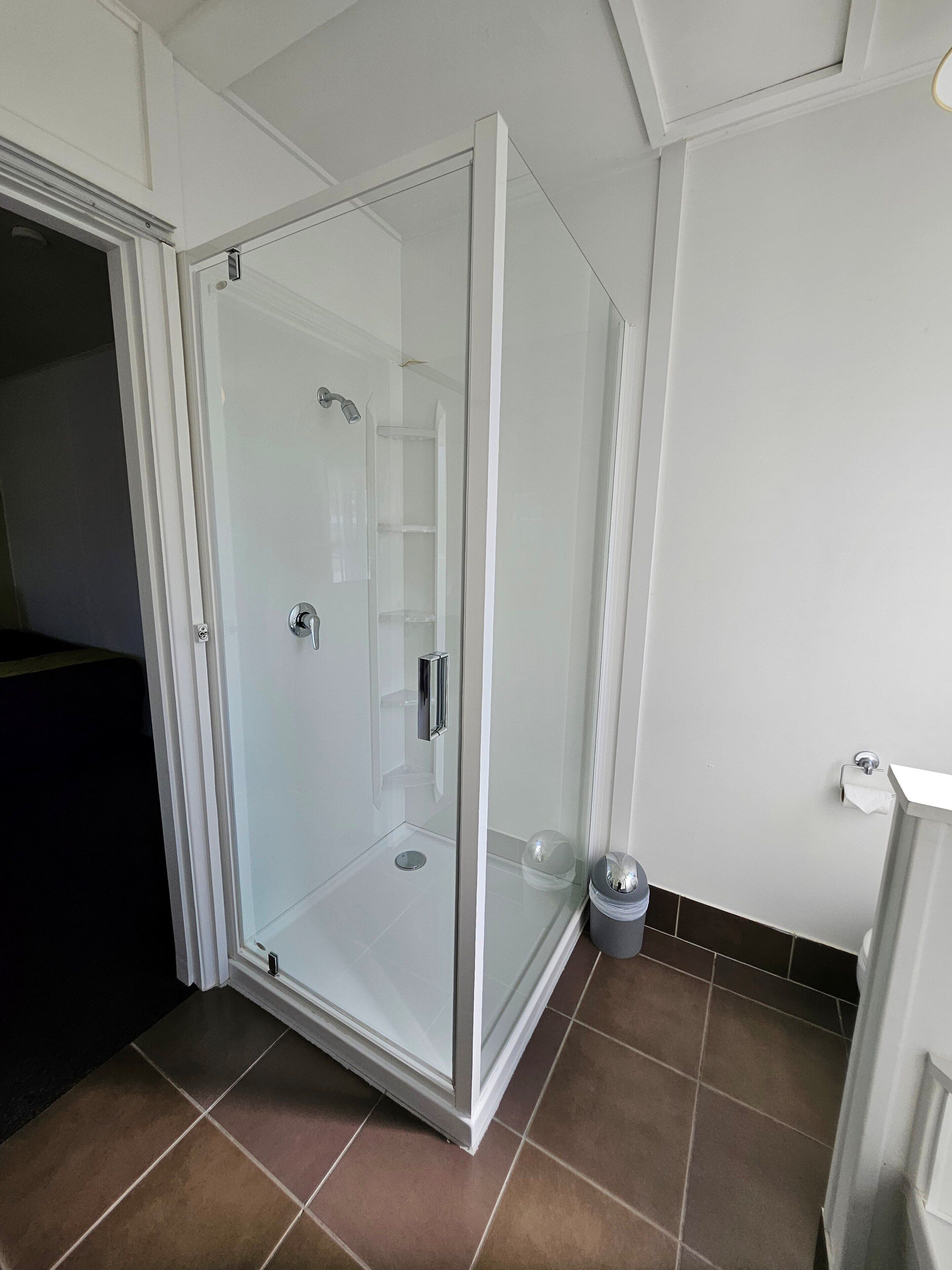 A glass-enclosed shower with a door, a trash bin, and a tiled floor.