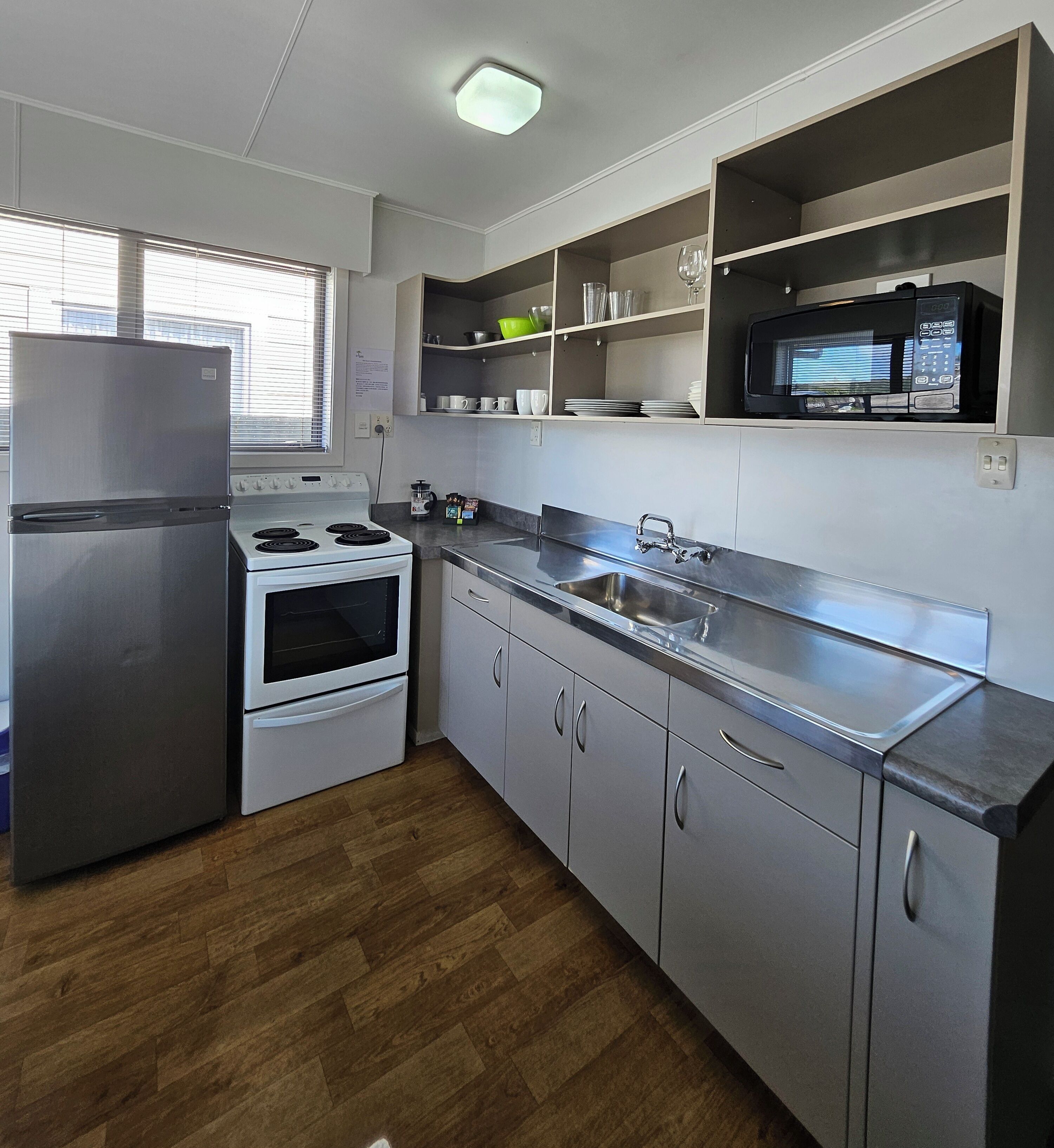 A modern kitchen with stainless steel appliances, wooden flooring, and built-in shelves.