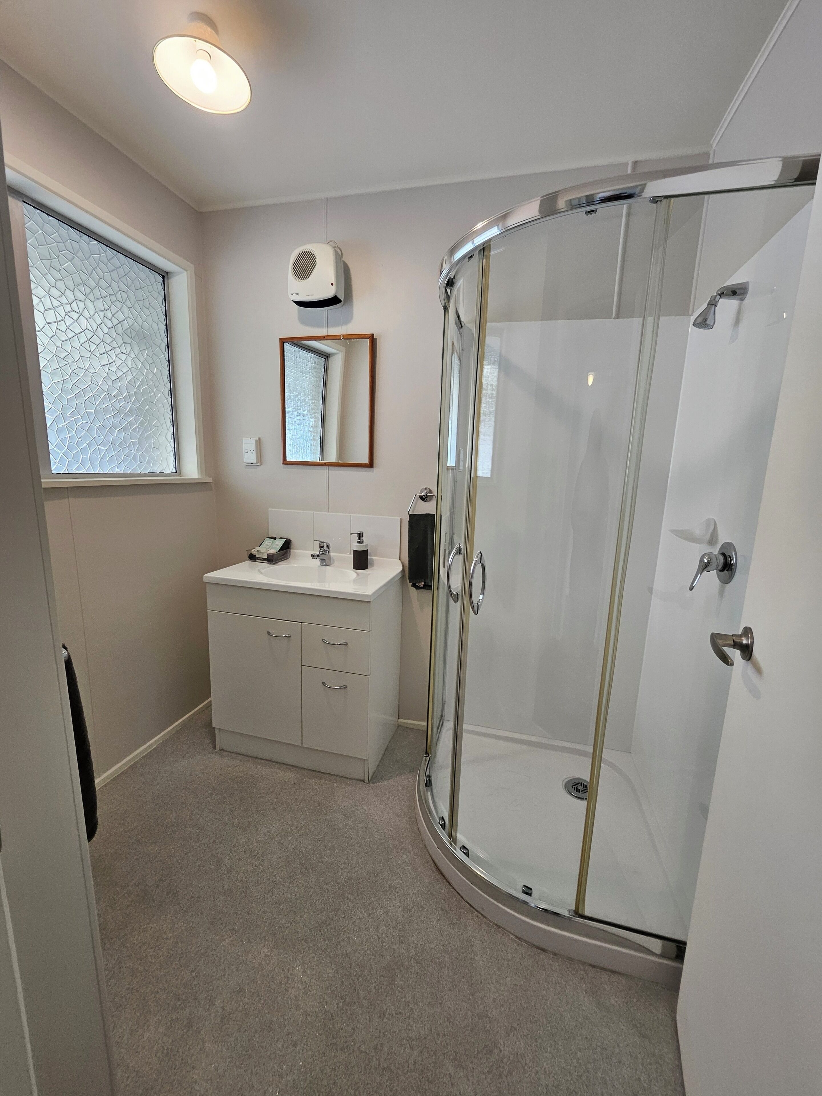 A bathroom with a glass-enclosed shower, a vanity with a mirror, and a window with a textured design.