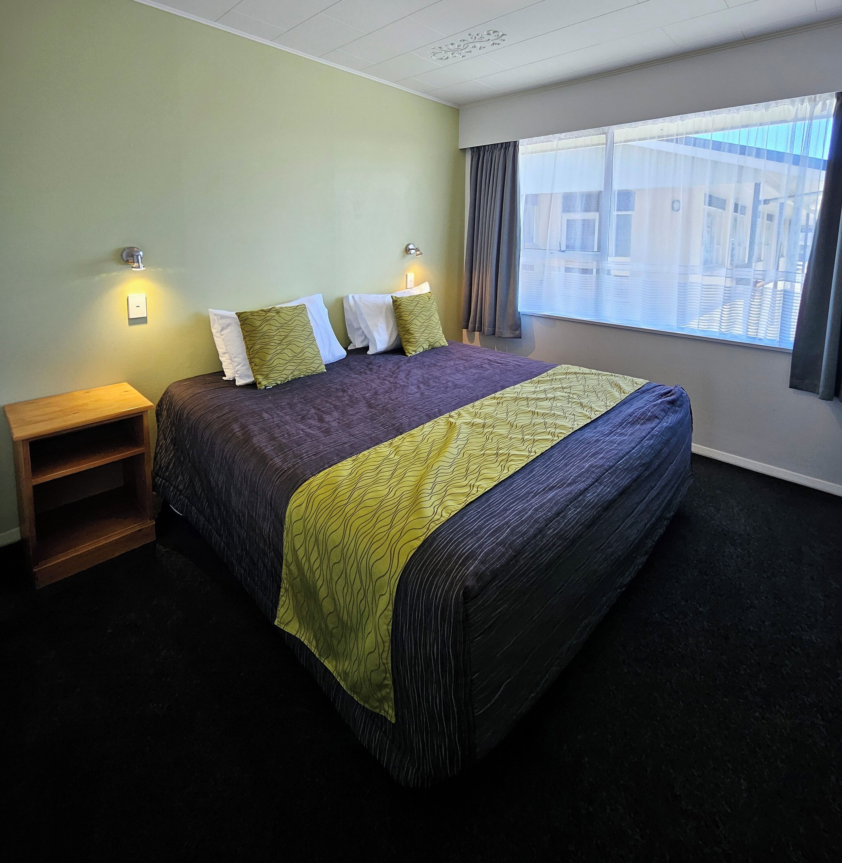 Habitación de hotel con cama, mesitas de noche, ventana con cortinas y vistas a edificios.