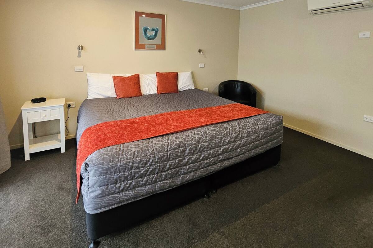 Quarto com cama, mesa de cabeceira, cadeira, ar condicionado e um quadro na parede.