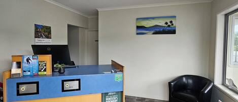 A reception desk with a blue top, a black chair, a painting on the wall, and a window with a view.
