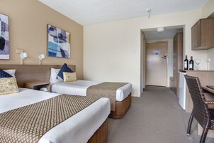 Une chambre d’hôtel avec deux lits, un bureau et une chaise. Les murs sont ornés de tableaux abstraits, et une porte donne accès à la salle de bain.