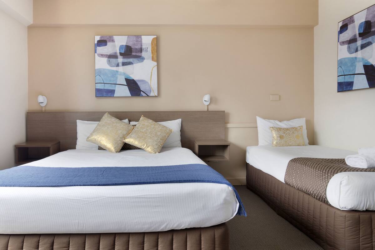 Quarto de hotel com duas camas, cada uma com um estilo diferente de cabeceira, e um grande quadro abstrato na parede.