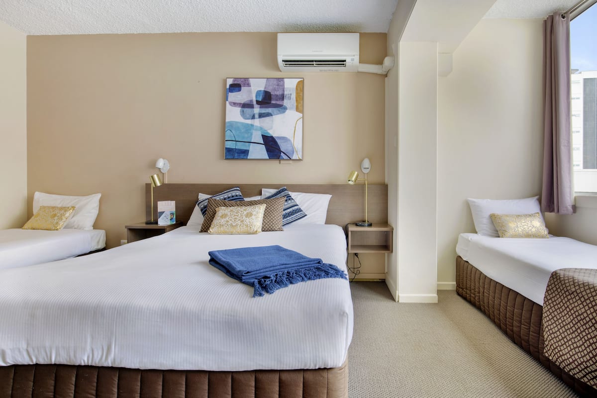 Quarto de hotel com uma cama grande, duas mesas de cabeceira, ar condicionado fixado na parede e uma janela com cortinas.