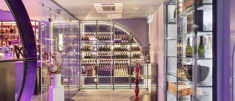 A modern hotel lobby with a wine cellar, a red cushioned seating area, and a glass display case with various items.
