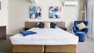 A hotel room with a large bed, two side tables, a blue armchair, and abstract artwork on the walls.