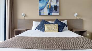 A hotel room with a large bed, two bedside tables, a wall-mounted abstract painting, and a window with curtains.